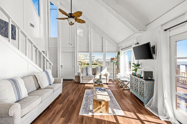 A spacious living room with a wooden floor, a white sofa, a coffee table, and a ceiling fan. - Hit the Beach (Galveston)