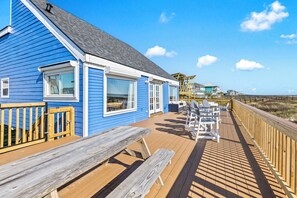 Ein blaues Gebäude mit einer Holzterrasse, Sitzgelegenheiten im Freien und Blick auf den Strand.