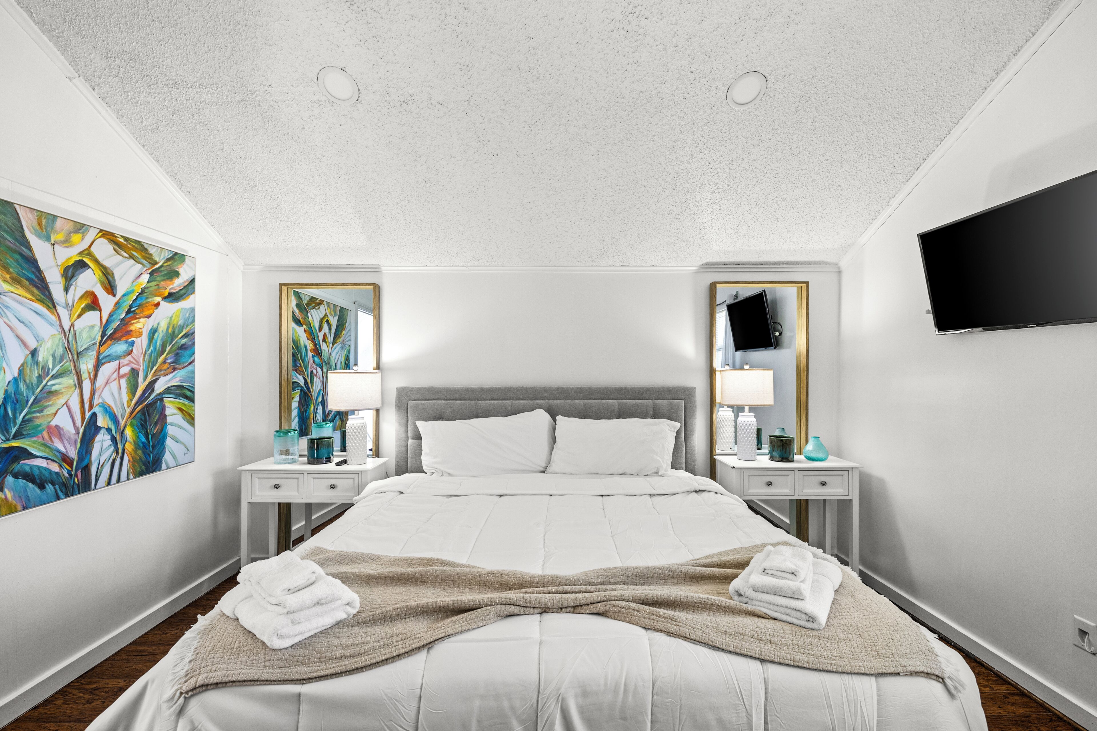 Une chambre d’hôtel moderne dotée d’un grand lit, de deux tables de chevet, d’un téléviseur à écran plat et d’un plafond équipé de spots encastrés.