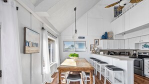 Una cocina con isla de madera, taburetes de bar blancos, una lámpara colgante y vistas al exterior a través de una ventana.