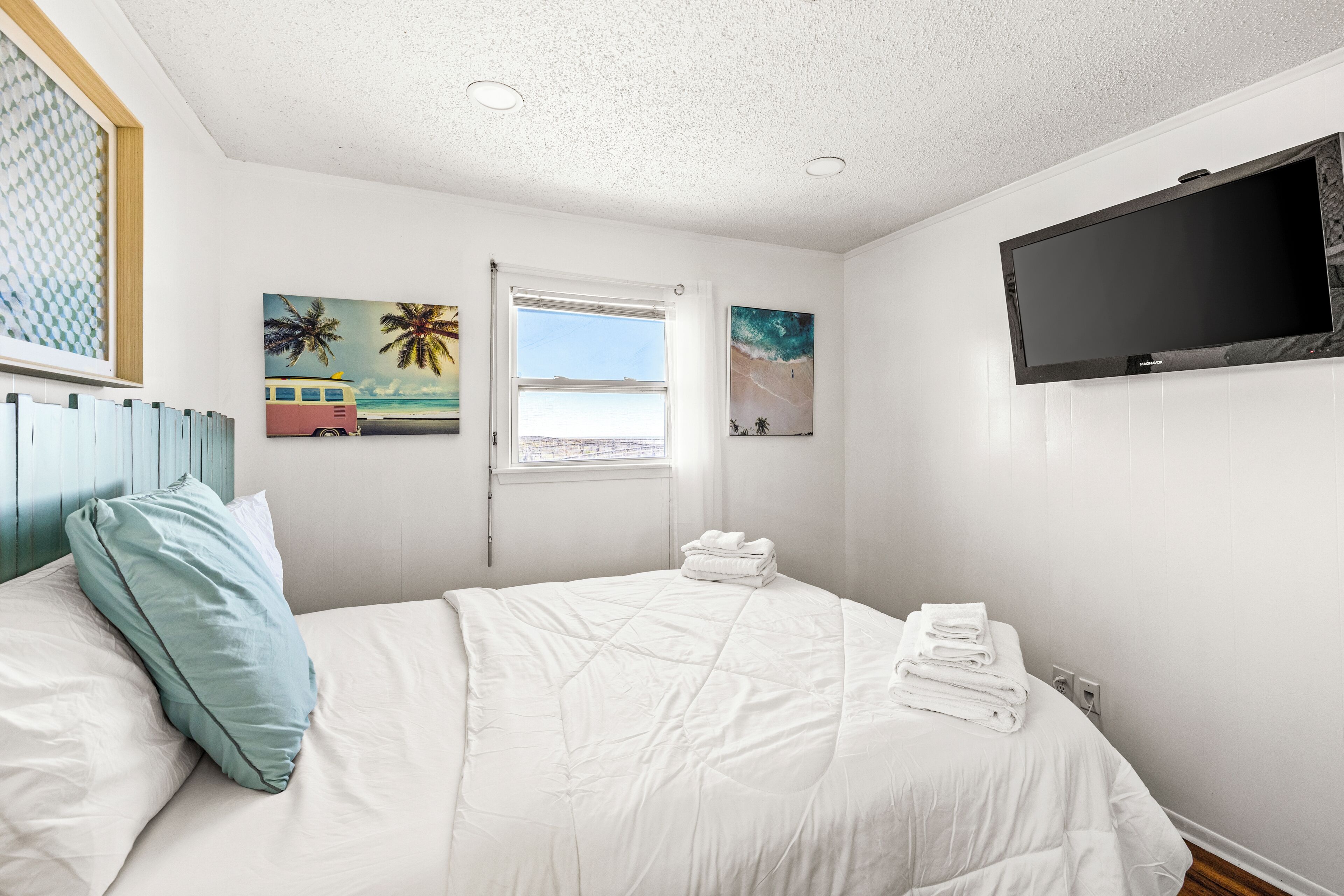 A bedroom with a bed, a window, a TV, and artwork on the wall.