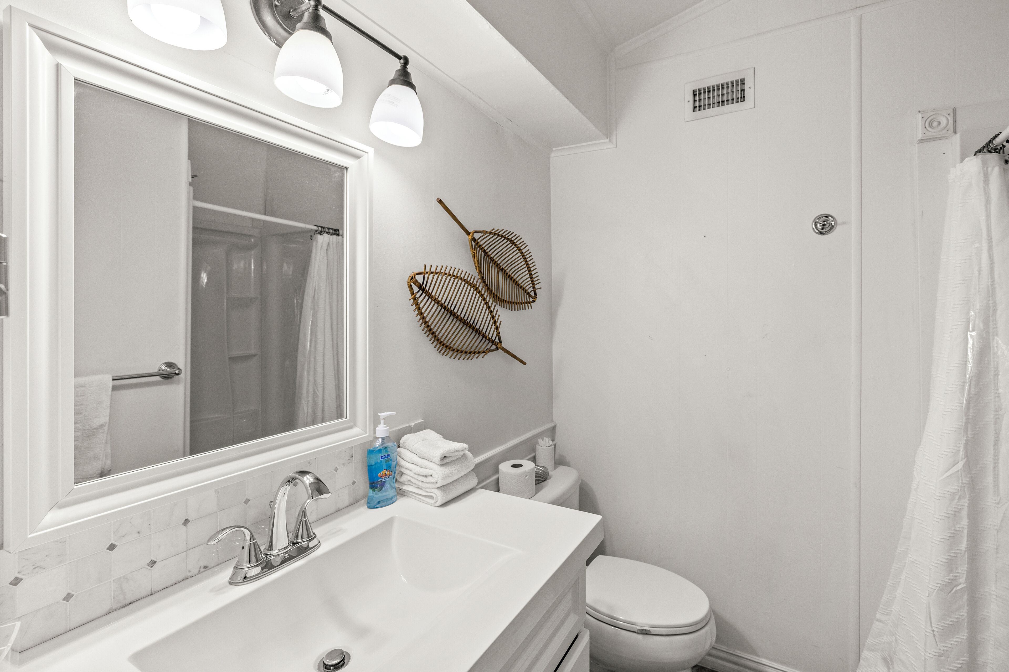 Une salle de bain avec un grand miroir, un lavabo, des toilettes et un rideau de douche.