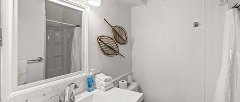 Une salle de bain avec un grand miroir, un lavabo, des toilettes et un rideau de douche.