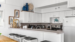 Una cocina moderna con armarios blancos, una isla central con taburetes, microondas, estufa y refrigerador.