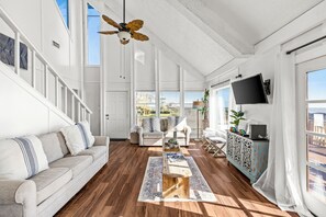 Un salon spacieux doté d’un plancher en bois, d’un canapé blanc, d’une table basse et d’un ventilateur de plafond.