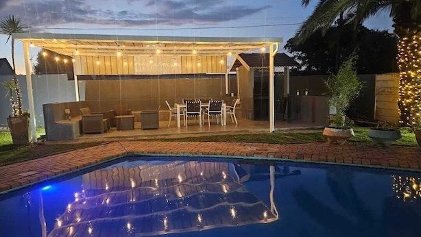 Un patio trasero con piscina, mobiliario exterior e iluminación con guirnaldas.