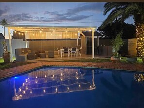 Un jardin avec une piscine, un espace salon extérieur et des guirlandes lumineuses.