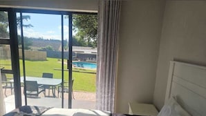 Habitación de hotel con cama, vista a una piscina y mobiliario exterior, además de una cortina.