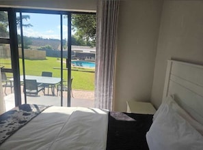 A hotel room with a bed, a view of a pool and outdoor seating, and a curtain.