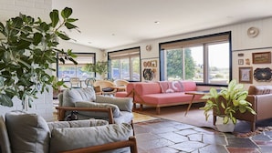 A spacious living area with a large window, a pink sofa, and several chairs. - Wayfinder Newport | Premium 2Queen | Local Art, Mural Pool, City by the Sea (Newport County)
