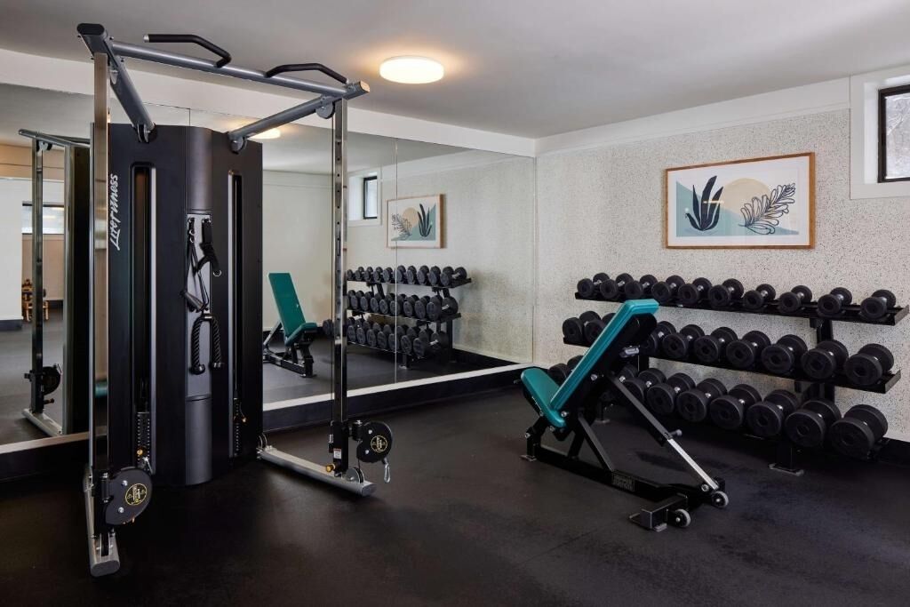 Een sportschool met gewichthefapparatuur, dumbbells en een spiegel.