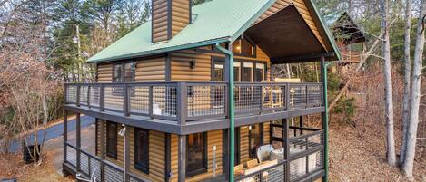 A two-story log cabin with a balcony, surrounded by trees.