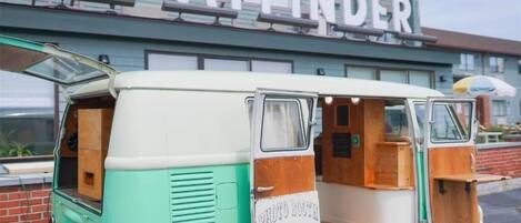 Uma carrinha antiga com interior de madeira, identificada como cabine fotográfica, estacionada em frente a um edifício com uma placa a dizer 'the WAYFINDER'.