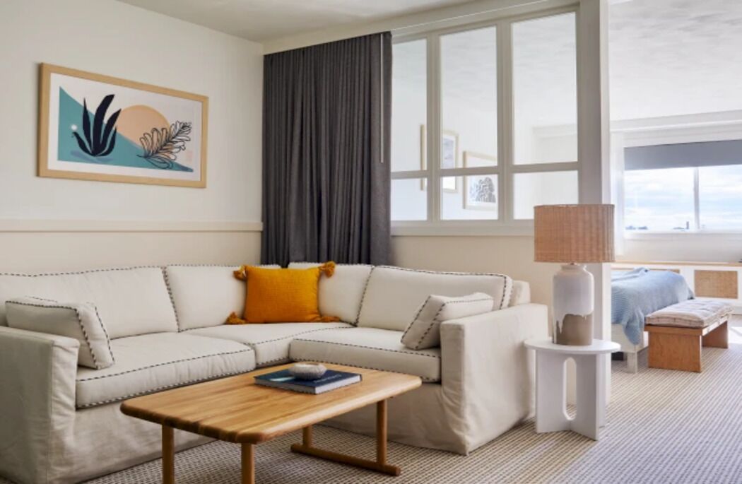 Uma sala de estar moderna com um sofá seccional, uma mesa de centro, um abajur e um quadro na parede.