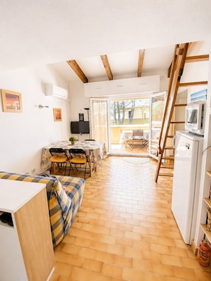 A compact living space with a dining area, a sofa, a TV, and a refrigerator. - EUREKA C43 - Appartement - Piscine - 100m Plages (Agde)