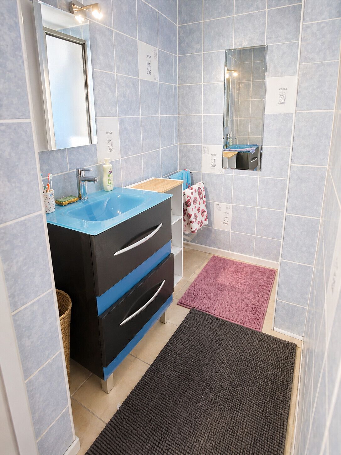 A bathroom with a blue sink, black and blue cabinet, a mirror, and a pink rug.