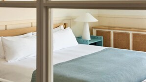 Quarto de hotel com cama, mesa de cabeceira, luminária e janela.
