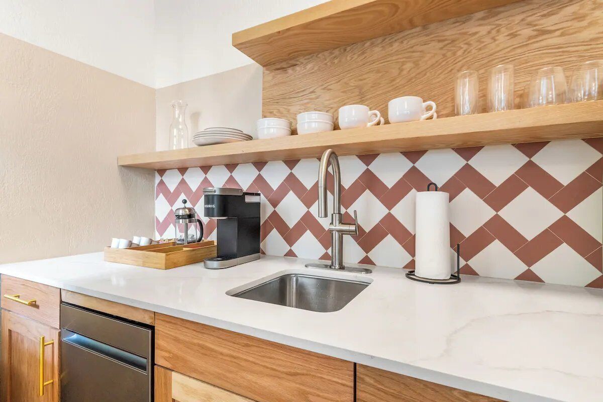 Una cocina moderna con un lavamanos de acero inoxidable, armarios de madera, una cafetera y un salpicadero con diseño.