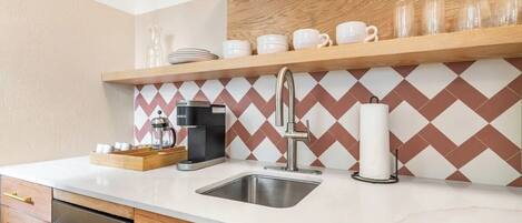 Una cocina moderna con un lavamanos de acero inoxidable, armarios de madera, una cafetera y un salpicadero con diseño.