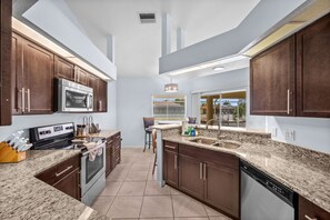 A modern kitchen with granite countertops, stainless steel appliances, and wooden cabinets. - Triple Palms Vacation Home, With Heated Pool (Cape Coral)