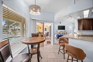 A modern kitchen with a dining area, a TV, and a large window with blinds. - Triple Palms Vacation Home, With Heated Pool (Cape Coral)