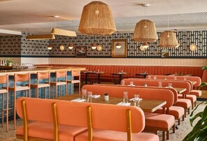 Un restaurant avec des banquettes et des tables orange, des suspensions décoratives en fibres tressées et des motifs décoratifs sur les murs.