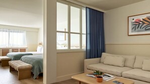 Una habitación con cama, sofá, ventana con cortinas, una mesita con una planta y un cuadro en la pared.