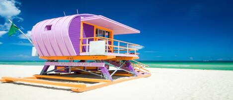 A lifeguard tower with 'MIAMI BEACH' written on it, situated on a sandy beach with clear blue water in the background.