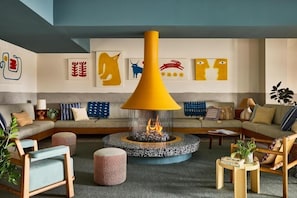 A modern living room with a central fireplace, sofas, and a coffee table. - 2 Queen Parlor | Wayfinder Newport | Authentic Newport, Local Art (Newport County)