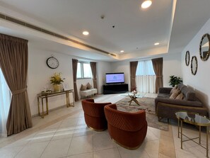 Ein modernes Wohnzimmer mit einer Couch, zwei Sesseln, einem Couchtisch, einem Fernseher und einer Wanduhr.