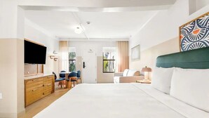 Ein Hotelzimmer mit einem Bett, einem Schreibtisch mit Stuhl, einem Fernseher und einem Fenster mit Vorhängen.