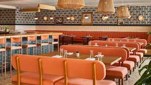 A restaurant with orange booths and tables, woven pendant lights, and patterned wall decor.