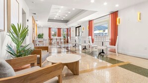 Eine Hotelhalle mit einer zentralen Sitzecke, einem Empfangsbereich und Blick ins Freie.