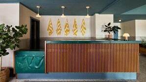 A reception desk with a green and blue color scheme, a wooden slatted design, and a wall-mounted light fixture. - 1BR Suite | Wayfinder Newport | Best of Both Worlds, Basecamp | 2 Units (Newport County)