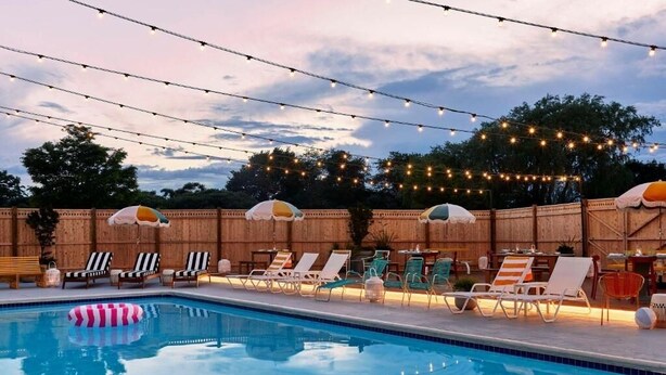 A swimming pool with lounge chairs and umbrellas, surrounded by string lights. - Wayfinder Newport | Wayfinder Suite | Boutique Cool, Local Art, Mural Pool (Newport County)