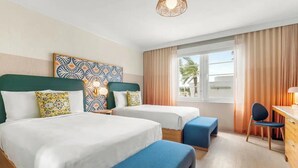 Una habitación de hotel con dos camas, un escritorio, una silla y un ventanal con cortinas.