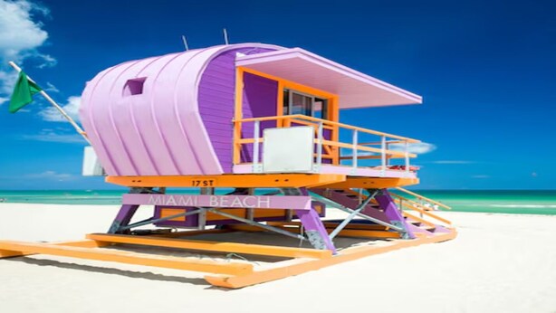 Een redershut met daarop 'MIAMI BEACH', gelegen op een zandstrand met helderblauw water op de achtergrond.
