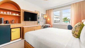 Hotelkamer met een bed, een televisie, een koffiezetapparaat, een kleine koelkast en een raam met gordijnen.