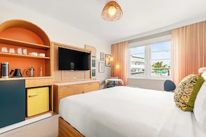 Habitación de hotel con cama, televisión, cafetera, refrigerador pequeño y ventana con cortinas.