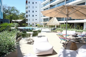 A rooftop pool area with lounge chairs, a thatched umbrella, and a modern building in the background. - Zonte Wave Watch - 2BR Surf & Work Retreat (El Zonte)