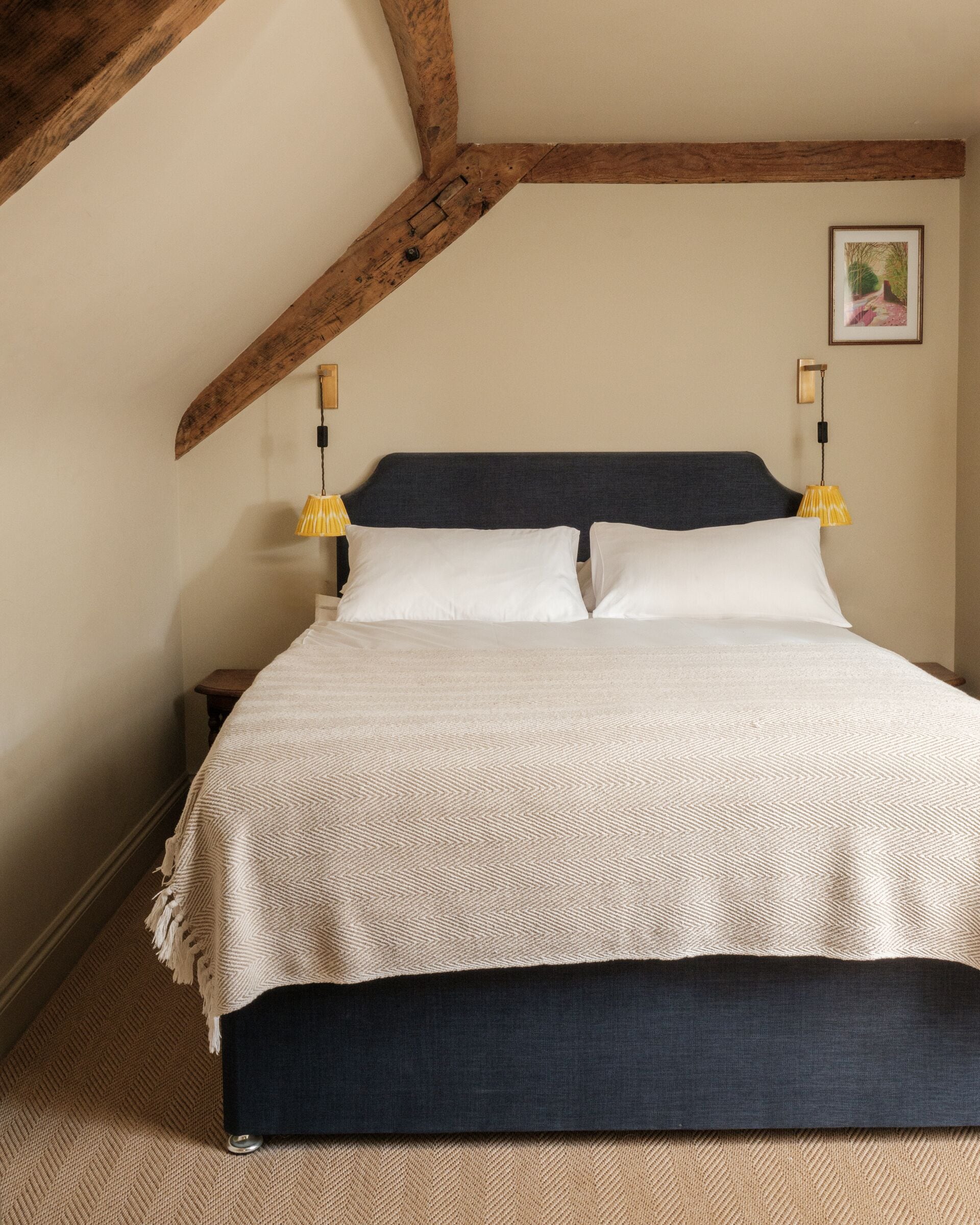 Una camera da letto con un letto, travi in legno, una lampada e un quadro appeso al muro.
