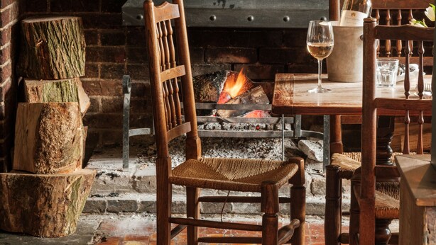 A rustic interior with a fireplace, wooden furniture, and a brick wall. - The Bell & Crown (Zeals)