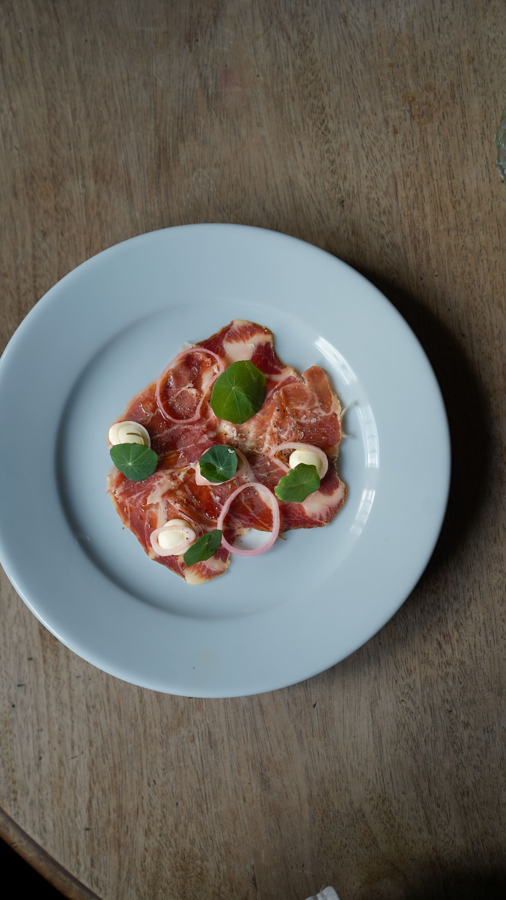 Une assiette de jambon de Parme, agrémentée de quelques accompagnements, posée sur une table en bois.