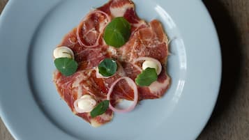 Une assiette de jambon de Parme, agrémentée de quelques accompagnements, posée sur une table en bois.
