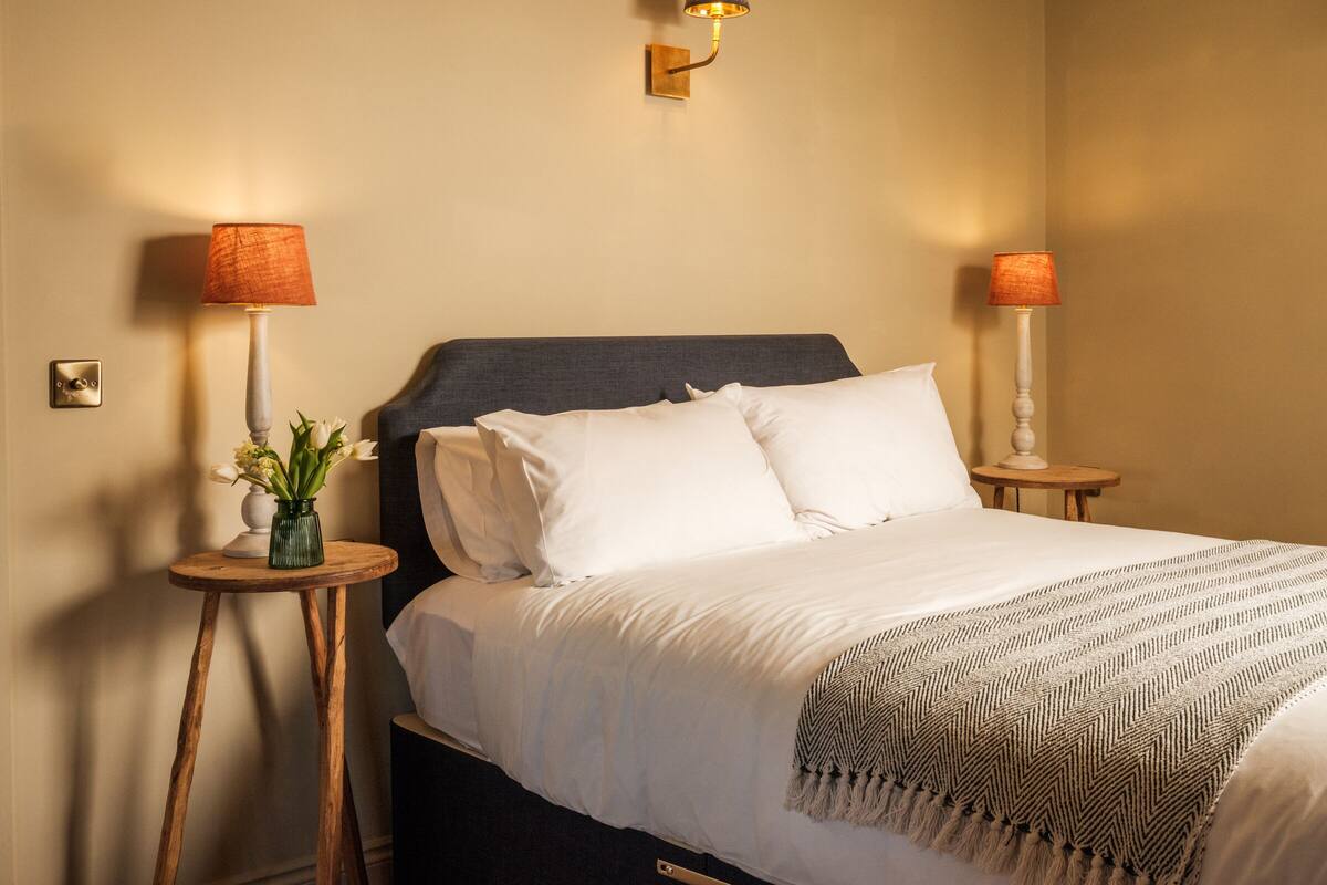 A neatly made bed with white linens, two bedside lamps, and a wall-mounted light fixture.