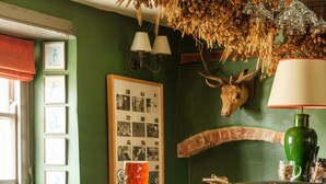 A bar area with stools, a green wall, framed pictures, and a mounted animal head. - The Bell & Crown (Zeals)