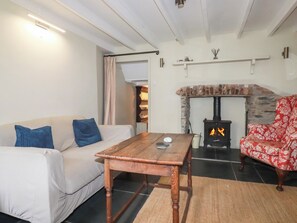 A cozy living room with a sofa, a wooden table, a patterned armchair, a fireplace, and a ceiling light. - Penvar (Truro)