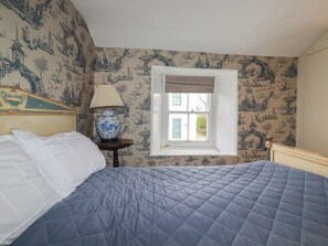 A bedroom with a bed, a window with a view, a lamp, and a wall with a patterned wallpaper. - Penvar (Truro)