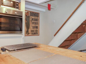 A kitchen with a stainless steel oven, a poster on the wall, and a wooden table with metal rods. - Penvar (Truro)