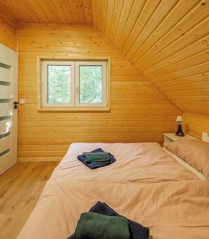 A small, cozy room with wooden walls and a sloped ceiling, featuring a bed with a single pillow and a bedside table with a lamp. - Leno Tu – Loft Cottage with Sauna and Hot Tub (Tuchomie)